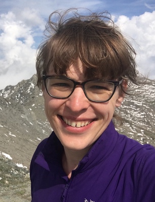 Selfie of a woman wearing a purple jacket in front of a rocky mountain in Queyras region, France